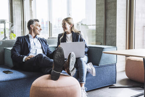 Glückliche Geschäftskollegen, die sich unterhalten und auf dem Sofa im Büro sitzen - UUF29855