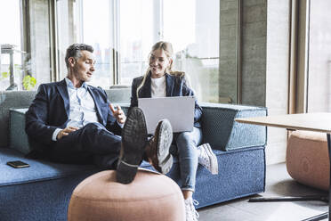 Fröhliche Geschäftskollegen, die im Büro am Laptop diskutieren - UUF29856