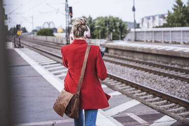 Woman wearing wireless headphones walking on platform - UUF29869