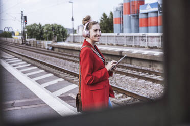 Happy woman with tablet PC standing on railroad station platform - UUF29871