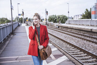 Smiling woman talking on smart phone at railroad station - UUF29872