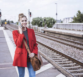 Happy woman talking on smart phone at railroad station - UUF29873