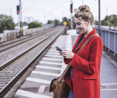 Happy woman using smart phone at railroad station - UUF29874