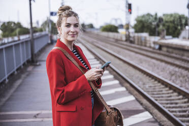 Lächelnde Frau mit Smartphone auf dem Bahnhof - UUF29875