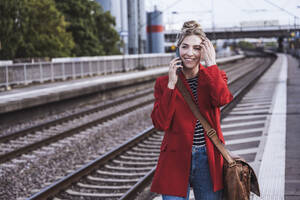 Glückliche Frau, die am Bahnhof mit einem Mobiltelefon spricht - UUF29876