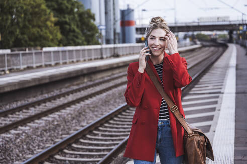 Happy woman talking on mobile phone at railroad station - UUF29876