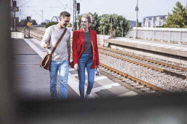 Lächelndes Paar beim gemeinsamen Spaziergang am Bahnhof - UUF29882