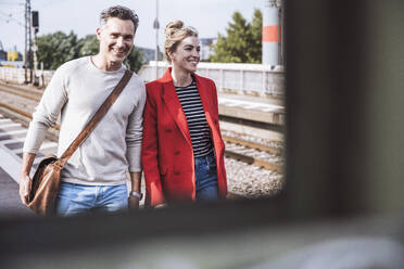 Lächelnder Mann und Frau gehen zusammen am Bahnhof spazieren - UUF29884