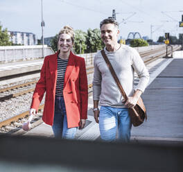 Lächelndes Paar, das gemeinsam auf dem Bahnsteig spazieren geht - UUF29886