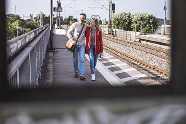 Glückliches Paar, das an einem sonnigen Tag gemeinsam auf dem Bahnsteig spazieren geht - UUF29887