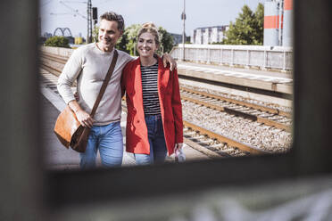 Lächelndes Paar, das an einem sonnigen Tag gemeinsam auf dem Bahnsteig spazieren geht - UUF29888
