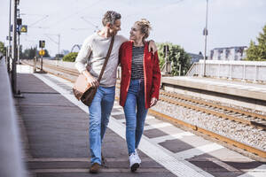 Glücklicher Mann und Frau gehen zusammen auf dem Bahnsteig an einem sonnigen Tag - UUF29889