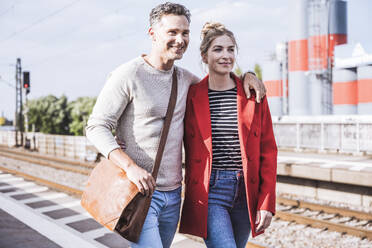 Lächelnder Mann und Frau, die an einem sonnigen Tag gemeinsam auf dem Bahnsteig spazieren gehen - UUF29890