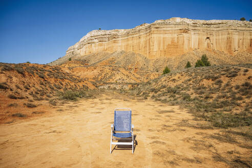 Left empty foldable fabric camp chair on plain sandy ground by rocky mountain canyon on sunny day at Canon Rojo Teruel Spain - ADSF46058