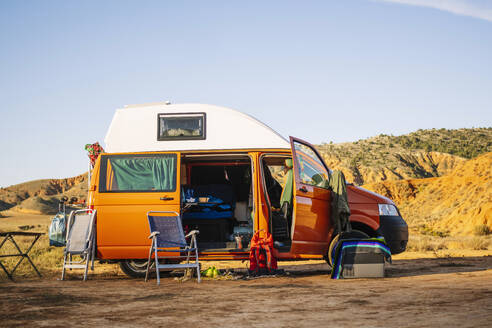 Modernes Wohnmobil mit klappbaren Sesseln und Kleidung geparkt durch hügeliges Gelände gegen wolkenlosen blauen Himmel an einem sonnigen Tag am Canyon Rojo Teruel Spanien - ADSF46066