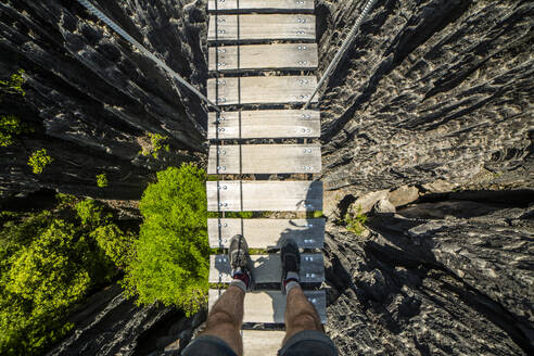 From above of anonymous male traveler standing on wooden planks of way bridge tied with ropes on valley of rock formation of park in Madagascar Africa - ADSF46075