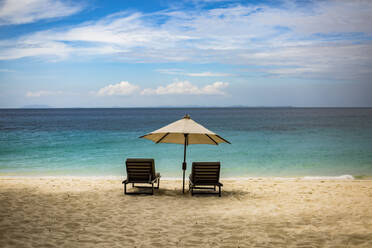 Pair of wooden sunbeds placed under summer umbrella on sandy coast of amazing ocean with turquoise water, Madagascar - ADSF46085