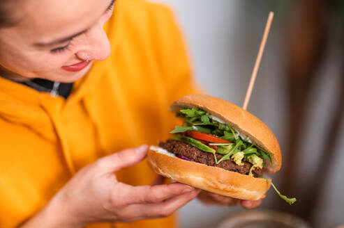 Crop positive young female in casual clothes with delicious burger in cafe - ADSF46134