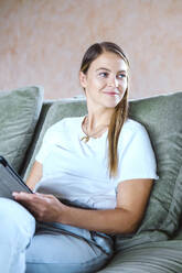 Smiling freelancer using tablet PC on sofa at home - YHF00023