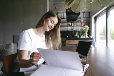 Smiling freelancer turning page of book at home - YHF00037