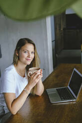 Smiling freelancer holding coffee cup at table - YHF00039