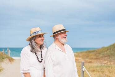 Ruhige ältere Frau im weißen Kleid und Mann im Hemd stehen am Sandstrand und schauen weg - ADSF46145