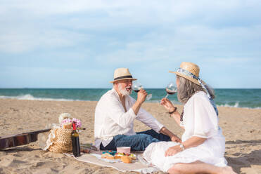 Positive man and woman in White clothes drinking in wine while having picnic on sandy coast - ADSF46154