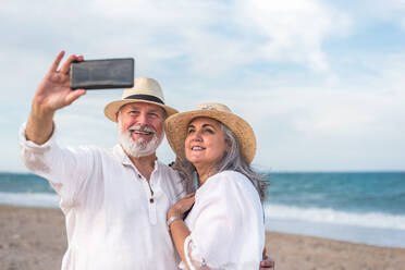 Ein älteres Paar genießt seine Zeit am Strand und hält seine Erinnerungen mit einem Selfie auf seinem Smartphone fest - ADSF46162