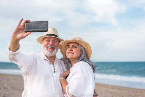 Ein älteres Paar genießt seine Zeit am Strand und hält seine Erinnerungen mit einem Selfie auf seinem Smartphone fest - ADSF46162