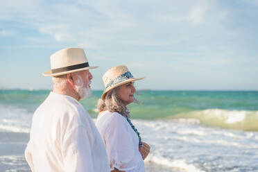 Seitenansicht ruhige ältere Frau in weißem Kleid und Mann im Hemd stehen am Sandstrand und schauen weg - ADSF46172