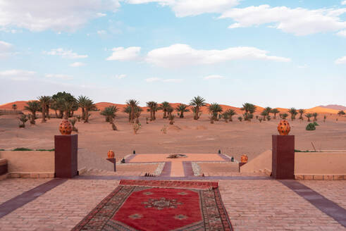 Ornamental carpet on terrace of luxury hotel entrance in Merzouga desert Morocco against cloudy sky - ADSF46174