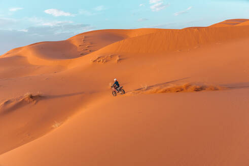 Side view of unrecognizable person riding motorbike on sand dune against cloudy sky in Merzouga desert Morocco - ADSF46182