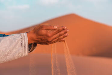 Side view of sand falling from cropped hands of anonymous person against blurred background in Merzouga desert Morocco on sunny day - ADSF46184