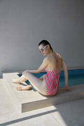 Junge Frau in gestreifter Badekleidung sitzt am Whirlpool - EKHF00058