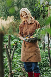 Glückliche Frau mit Gemüsekorb im Garten - VSNF01267
