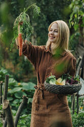 Glückliche Frau, die eine Karotte im Garten untersucht - VSNF01271