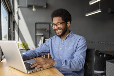 Smiling businessman working on laptop in office - VRAF00127