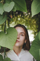 Woman covering eye with leaf in garden - YTF00915
