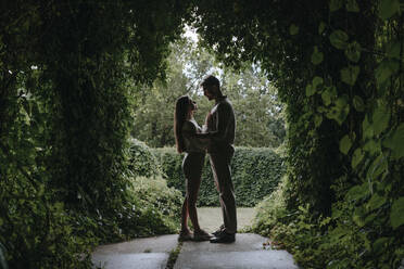 Junges Paar steht unter Pflanzenbogen im Garten - YTF00924