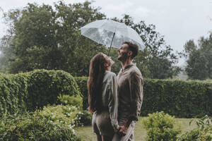 Glückliches Paar hält Regenschirm und genießt den Regen im Garten - YTF00928
