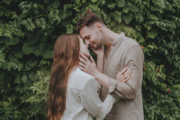 Smiling couple kissing in front of plants in garden - YTF00944