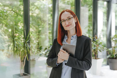 Lächelnde rothaarige Geschäftsfrau stehend mit Tablet-PC im Büro - YTF00954