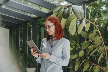 Smiling redhead businesswoman wearing eyeglasses using tablet PC - YTF00961