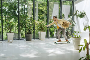 Glücklicher Geschäftsmann beim Longboard-Skaten im Büro - YTF00964