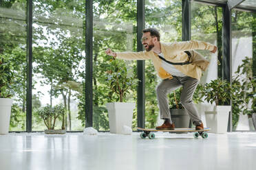 Cheerful businessman doing longboard skating in front of window - YTF00966