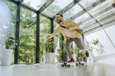 Happy businessman enjoying longboard skating in office - YTF00967