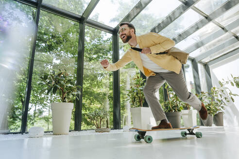 Cheerful businessman enjoying longboard skating in office - YTF00968