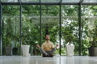 Businessman meditating with eyes closed in front of window - YTF00976