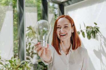 Happy businesswoman looking at light bulb in office - YTF00983