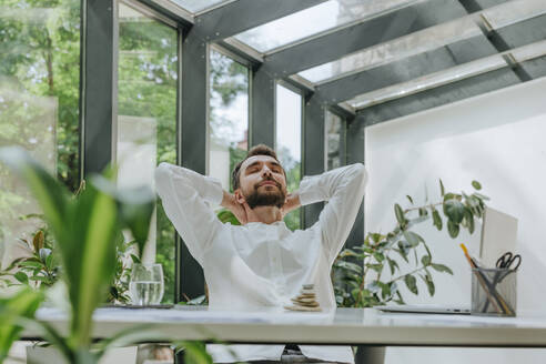 Businessman relaxing with hands behind head in office - YTF01017